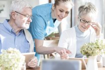 Senior adults using tablet computers in care home with nurse helping. — Stock Photo