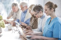 Adultos mayores en el hogar de cuidado usando tabletas con un trabajador de cuidado usando una computadora portátil . - foto de stock