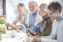 Senior adults in care home using tablet computers at table with drinks. — Stock Photo