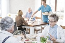 Adultos mayores desayunando en un hogar de cuidados mientras el cuidador sirve té . - foto de stock