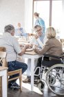 Mujer en silla de ruedas con amigos mayores desayunando en casa de cuidados . - foto de stock