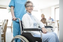 Infirmière poussant une femme âgée en fauteuil roulant dans une maison de soins . — Photo de stock