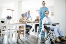 Senior mulher em cadeira de rodas posando com o trabalhador de cuidados em casa de cuidados . — Fotografia de Stock