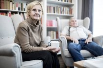 Senior couple sitting in armchairs in living room. — Stock Photo