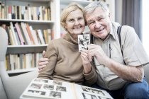 Senior couple posing with photograph from photo album. — Stock Photo