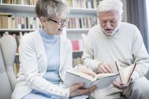 Seniorenpaar sitzt drinnen und liest Bücher. — Stockfoto