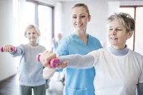 Seniorin mit Handgewicht hilft Physiotherapeutin. — Stockfoto