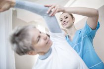Senior woman stretching with physiotherapist helping, low angle view. — Stock Photo
