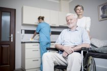 Senior man sitting in wheelchair with women in care home. — Stock Photo