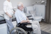 Senior woman pushing senior man in wheelchair in care home. — Stock Photo