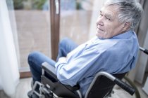 Homem sênior sentado em cadeira de rodas pela janela em casa de cuidados . — Fotografia de Stock