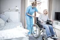 Senior woman in wheelchair talking with worker in care home. — Stock Photo