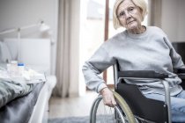 Mujer mayor en silla de ruedas por cama con medicación en el hogar de cuidados . - foto de stock