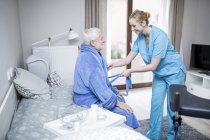 Care worker helping senior man putting on dressing gown. — Stock Photo