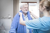 Care worker helping senior man putting on dressing gown. — Stock Photo