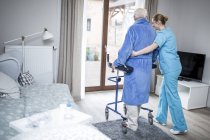 Pflegekraft hilft Seniorin beim Gehen mit Rollator. — Stockfoto