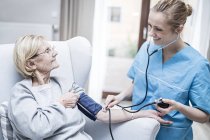 Enfermera que toma la presión arterial de la mujer mayor . - foto de stock
