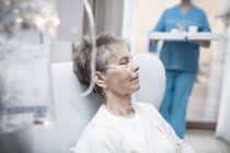 Mujer mayor con cánula nasal y bolsa IV y bandeja de sujeción de enfermera en segundo plano . - foto de stock