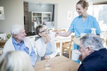 Female caregiver serving tea to senior adults in care home. — Stock Photo