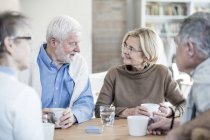 Senior friends talking at table with cups and glass of water in retirement home. — Stock Photo