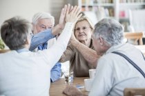 Friends giving high fives while sitting at table in retirement home. — Stock Photo