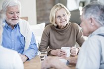 Senior friends talking in retirement home at table with drinks. — Stock Photo