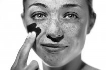 Young woman with freckles applying sunscreen to cheek. — Stock Photo
