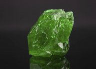 Green mineral gemstone on mirror surface. — Stock Photo