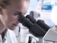 Jeune femme scientifique regardant le microscope pendant la recherche . — Photo de stock