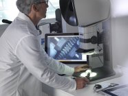 Male engineer using stereo microscope for inspecting manufactured component during quality control process. — Stock Photo
