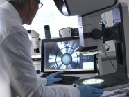 Ingeniero masculino que usa microscopio estéreo para inspeccionar componentes manufacturados durante el proceso de control de calidad
. - foto de stock