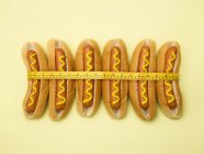Measuring tape around hot dogs on yellow background. — Stock Photo
