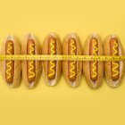 Measuring tape around hot dogs on yellow background. — Stock Photo