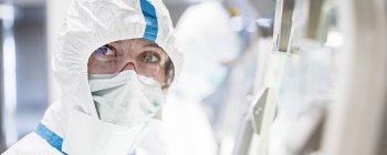 Лаборант в защитном костюме, маске для лица и защитных очках в стерильной лаборатории . — стоковое фото