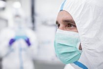Close-up of male lab technician in protective suit and face mask in sterile laboratory. — Stock Photo