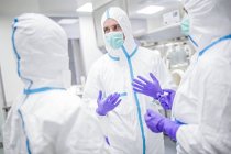Techniciens de laboratoire en combinaisons et masques de protection discutant dans un environnement de laboratoire stérile
. — Photo de stock