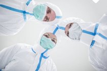 Técnicos de laboratorio en trajes de protección y máscaras mirando en cámara en laboratorio estéril . - foto de stock