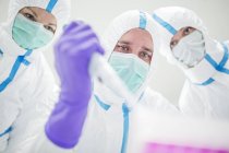 Tecnici di laboratorio in tute protettive e maschere pipettatura in laboratorio sterile . — Foto stock