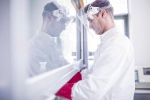 Lab technician using laminar flow hood, thick gloves and face shield while working with dangerous chemicals. — Stock Photo