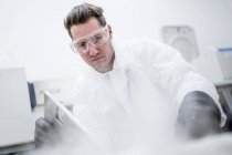 Male technician in safety goggles opening steaming cryostorage. — Stock Photo