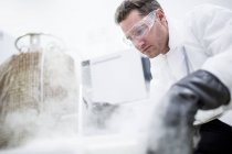 Male technician in safety goggles opening steaming cryostorage. — Stock Photo