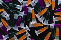 PCR tubes with orange, green and purple samples on black background. — Stock Photo