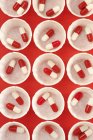 Vue du dessus des pots de médicaments en papier avec capsules de médicaments rouges et blanches . — Photo de stock