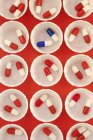 Paper medicine pots with red and white drug capsules and single dose of blue and white capsules. — Stock Photo