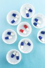 Papier-Medikamententöpfe mit blauen und weißen Kapseln und Einzeldosis roter und weißer Kapseln. — Stockfoto