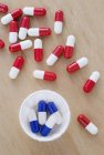 Cápsulas de drogas vermelhas e brancas e azuis e brancas em copo de papel e mesa de madeira . — Fotografia de Stock