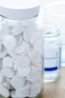 Белые круглые таблетки в стеклянной бутылке на столе . — стоковое фото