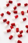 Червоні та білі капсули ліків розкидані на білому тлі . — стокове фото