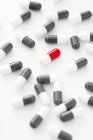 Cápsula roja y blanca rodeada de píldoras blancas y negras dispersas sobre fondo blanco
. - foto de stock