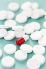 Round white pills surrounding oval red and white capsule. — Stock Photo
